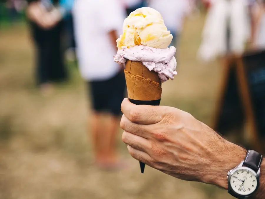 A hand holding a double-scoop gelato cone outdoors
